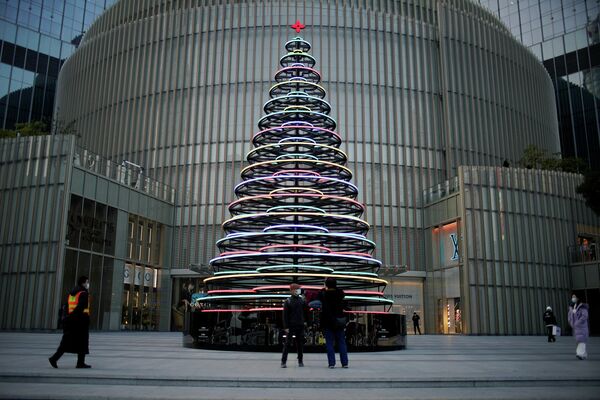 Люди стоят возле зажженной рождественской елки у торгового центра в Шанхае, Китай