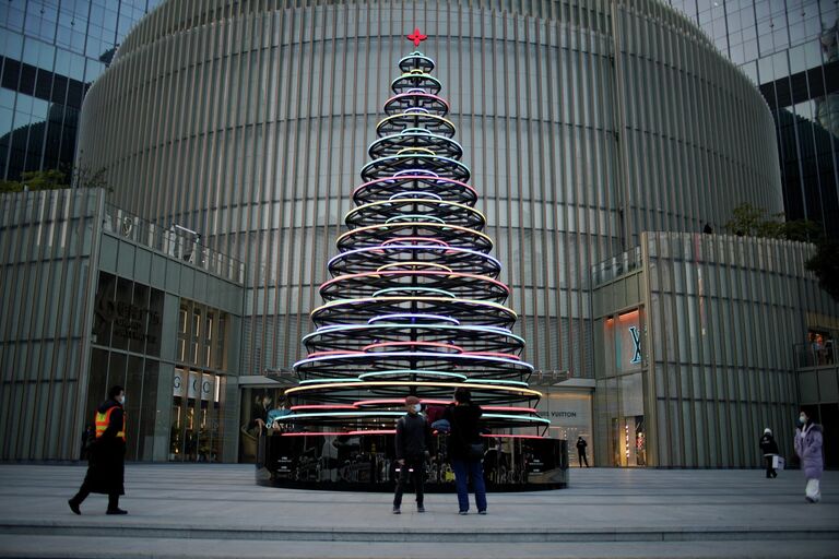 Люди стоят возле зажженной рождественской елки у торгового центра в Шанхае, Китай