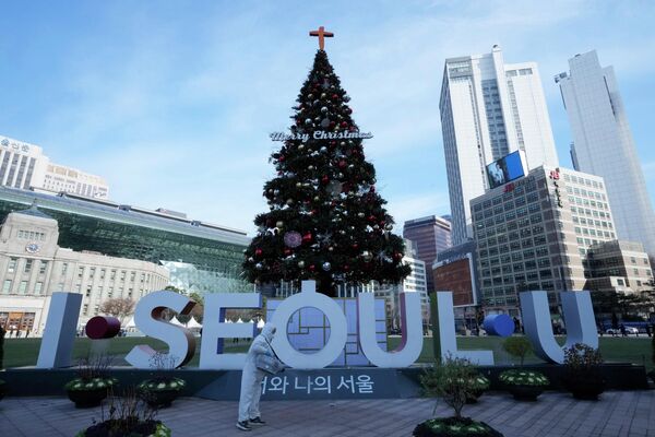 Мужчина в защитном снаряжении распыляет дезинфицирующее средство вокруг елки в качестве меры предосторожности против коронавируса в Сеуле, Южная Корея