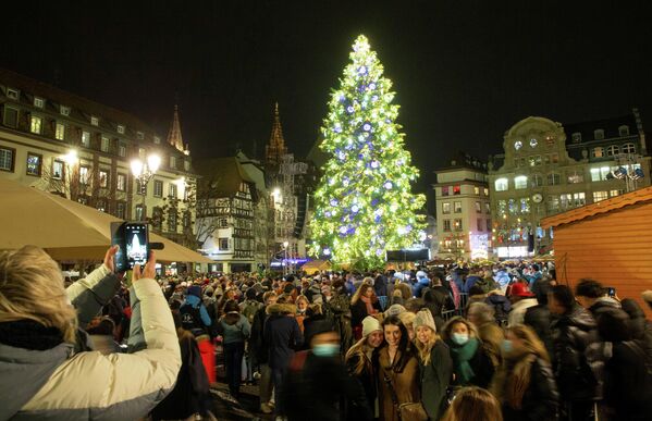 Люди вокруг освещенной елки на рождественской ярмарке на площади Клебер в Страсбурге, Франция