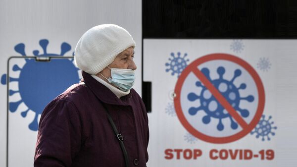 Женщина в защитной маске у информационного плаката Стоп CoVID-19 на улице Симферополя