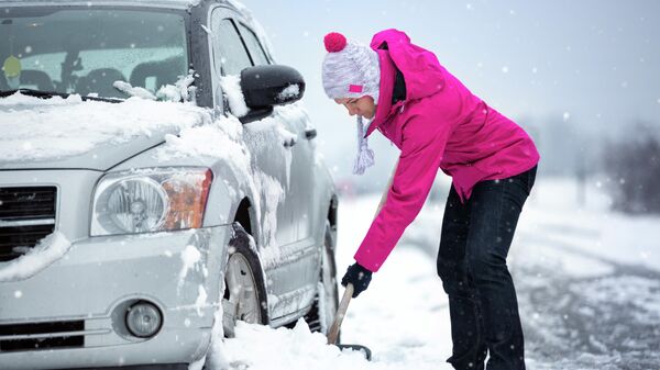 Женщина расчищает колеса автомобиля от снега
