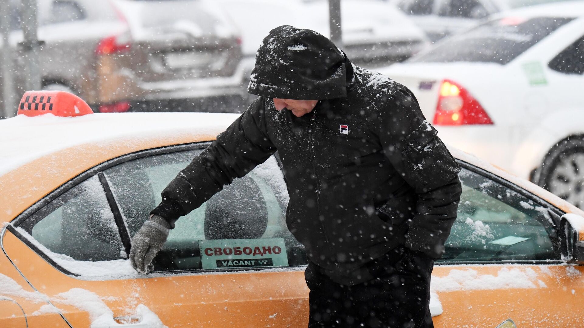 Водитель такси очищает автомобиль от снега во время снегопада в Москве - РИА Новости, 1920, 21.01.2022