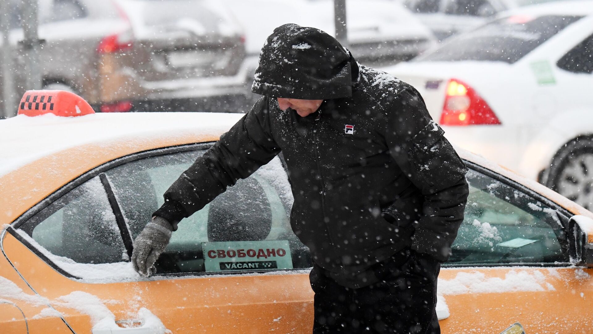 Водитель такси очищает автомобиль от снега во время снегопада в Москве - РИА Новости, 1920, 15.12.2023