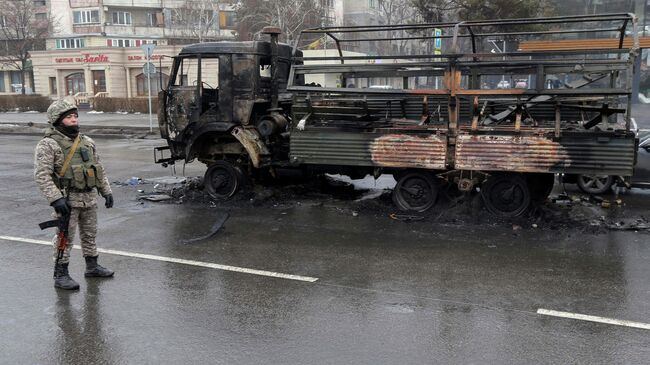 Военный возле сгоревшего грузовика на одной из улиц в Алма-Ате