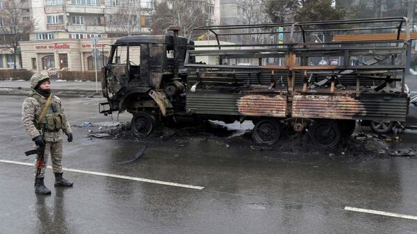 Сотрудник правоохранительных органов Казахстана возле сгоревшего грузовика в Алма-Ате