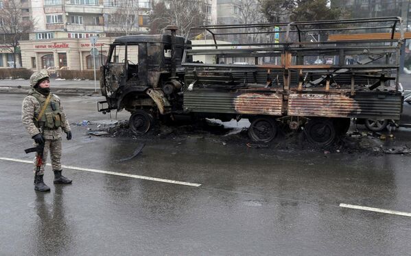 Сотрудник правоохранительных органов Казахстана возле сгоревшего грузовика в Алма-Ате