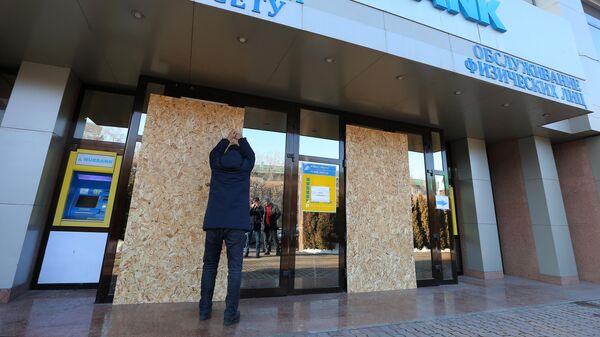 Мужчина закрывает плитой ДВП разбитое окно офиса Нурбанка в Алма-Ате