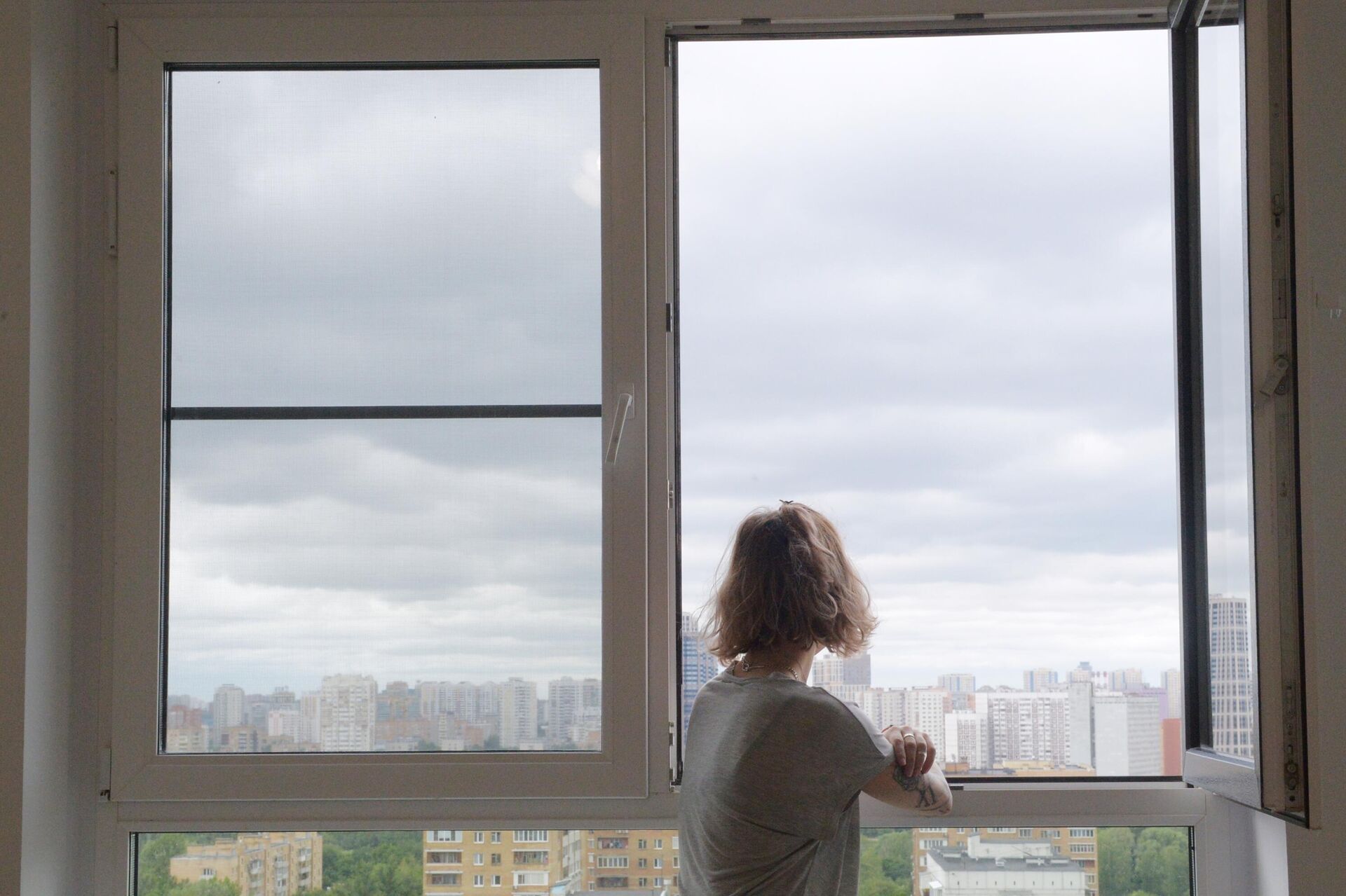 Девушка смотрит в окно в одной из квартир многоэтажного жилого дома - РИА Новости, 1920, 16.03.2022