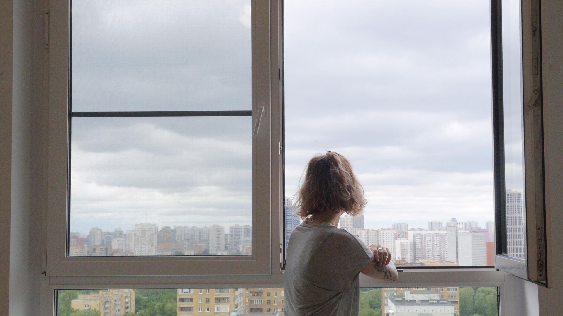 Девушка смотрит в окно в одной из квартир многоэтажного жилого дома - РИА Новости, 1920, 30.03.2022