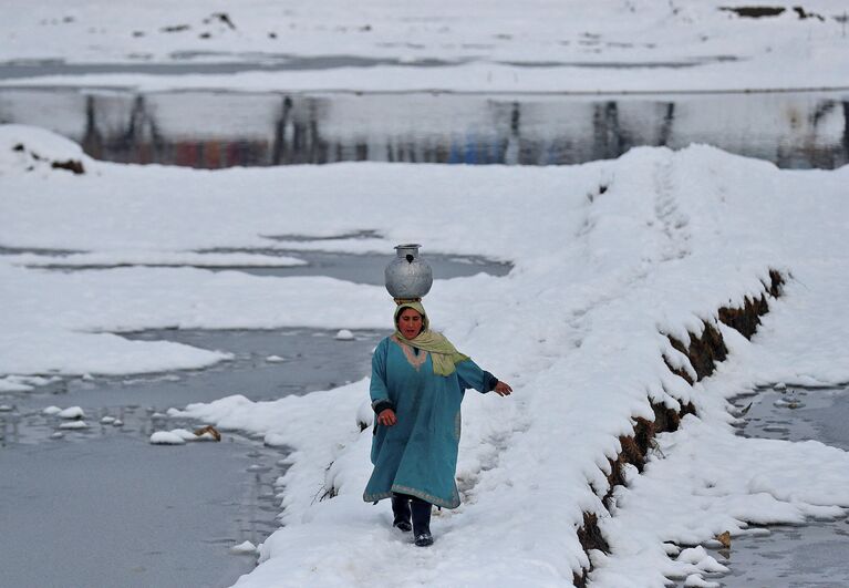 Женщина несет сосуд с водой по заметенному снегом полю в Сринагаре, Индия 