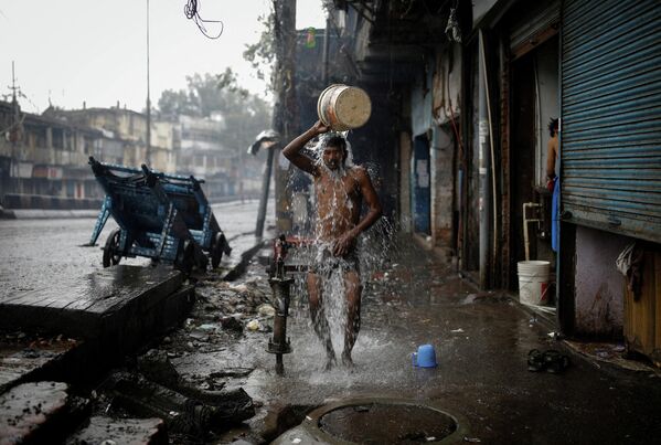 Мужчина моется из колонки на обочине дороги в Нью-Дели, Индия 