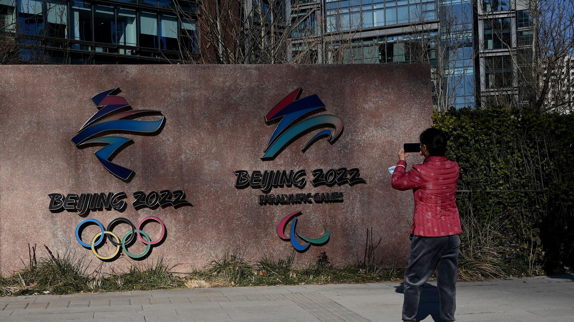 A woman takes a photo of the logos of Beijing 2022 Winter Olympics and Paralympic Winter Games in Shougang Park, one of the sites for the Olympics, in Beijing on December 7, 2021. (Photo by Noel Celis / AFP) - РИА Новости, 1920, 14.01.2022