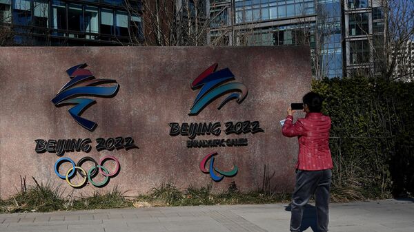 A woman takes a photo of the logos of Beijing 2022 Winter Olympics and Paralympic Winter Games in Shougang Park, one of the sites for the Olympics, in Beijing on December 7, 2021. (Photo by Noel Celis / AFP)