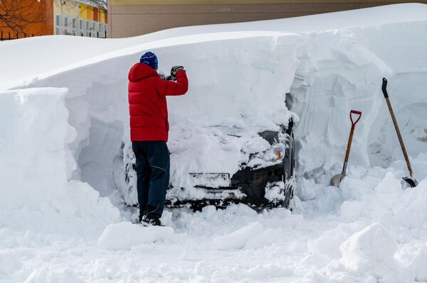 Мужчина расчищает из-под снега свой автомобиль на одной из улиц в Южно-Сахалинске