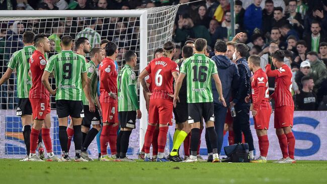 Sevilla's Spanish midfielder Joan Jordan Moreno (C) receives assistance after being hit by an object thrown from the tribunes during the Spanish Copa del Rey (King's Cup) round of 16 first leg football match between Real Betis and Sevilla FC at the Benito Villamarin stadium in Seville on January 15, 2022. - The Copa del Rey match between rivals Sevilla and Real Betis was stopped after Sevilla's Joan Jordan was struck on the head by an object thrown from the crowd. (Photo by CRISTINA QUICLER 