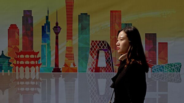 Женщина проходит мимо рекламного щита с изображением небоскребов в центральном деловом районе Пекина