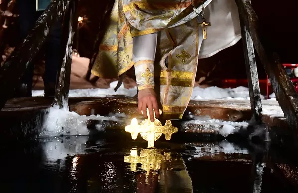 Священнослужитель окунает распятие в купель в Троицком административном округе Москвы  в праздник Крещения Господня
