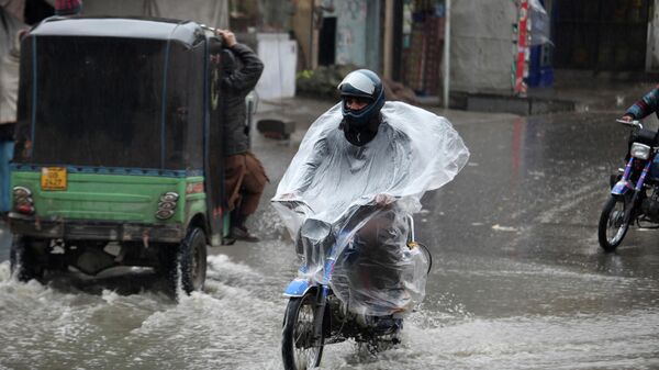 Мужчина едет на мотоцикле во время дождя в городе Пешавар, Пакистан