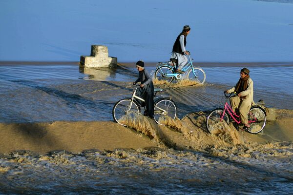 Мальчики катаются на велосипедах по воде  вышедшего из берегов ручья в Кандагаре 