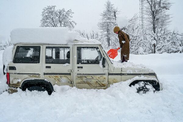 Мальчик расчищает снег с автомобиля после снегопада в Кашмире