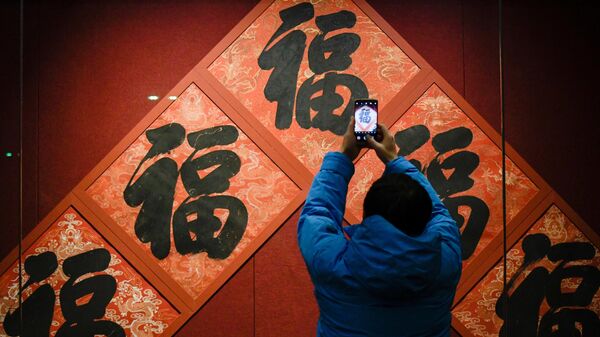 Мужчина фотографирует китайский иероглиф фу на выставке в Запретном городе в преддверии празднования китайского Нового года