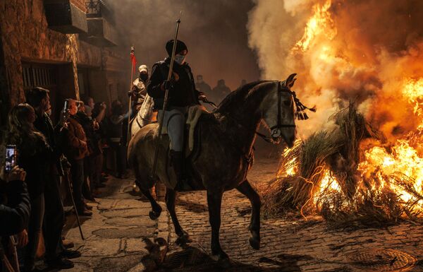 Женщина едет на лошади рядом с костром во время традиционного праздника Люминариас в деревне Сан-Бартоломей де Пинаре в Испании
