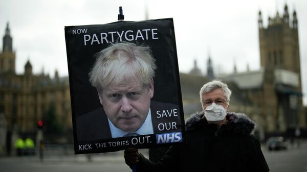 Протестующий с плакатом  с изображением Бориса Джонсона и надписью А теперь partygate около здания Парламента в Лондоне 