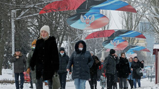 Люди проходят мимо флага и герба ДНР в Донецке