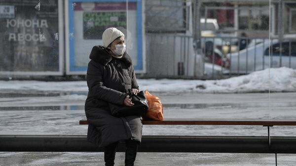 Пожилая женщина в защитной маске на остановке общественного транспорта в Симферополе