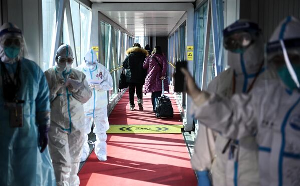 Медицинские сотрудники в защитных костюмах на телескопическом трапе в аэропорту Шоуду в Пекине