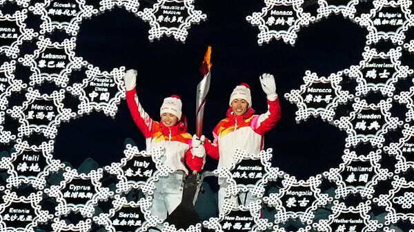 Спортсмены сборной КНР Динигир Йиламуцзян и Чжао Цзявэнь зажигают олимпийский огонь на церемонии открытия XXIV зимних Олимпийских игр в Пекине