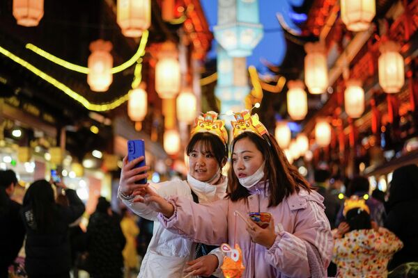 Девушки фотографируются во время фестиваля фонарей в саду Юйюань, Шанхай