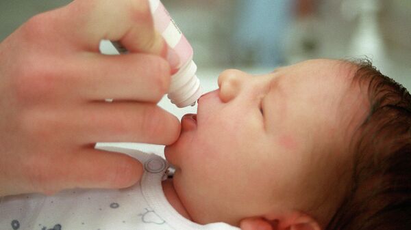 Акушерка дает новорожденному ребенку несколько капель витамина D3