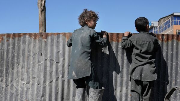 Афганские мальчики смотрят через забор на раздачу гуманитарной помощи нуждающимся семьям в Кабуле