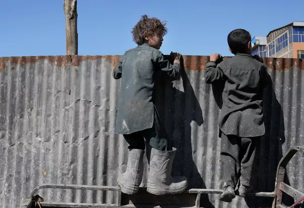 Афганские мальчики смотрят через забор на раздачу гуманитарной помощи нуждающимся семьям в Кабуле