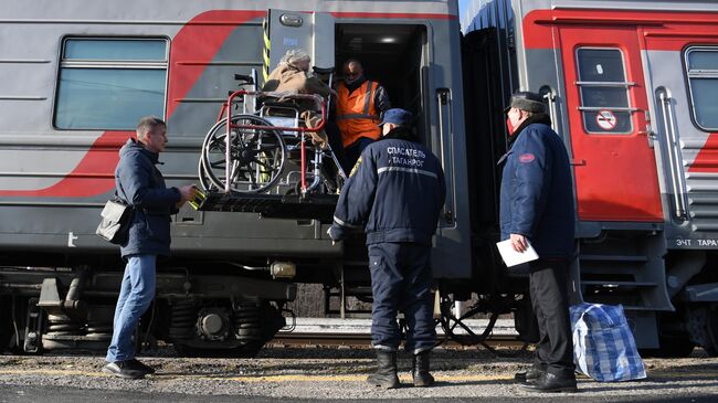 Сотрудники МЧС и РЖД помогают женщине сесть в поезд на железнодорожном вокзале Таганрог-1 в Ростовской области