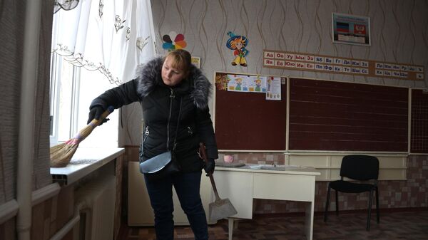 Женщина убирает осколки окон поврежденных в результате обстрела здания школы в  Донецке