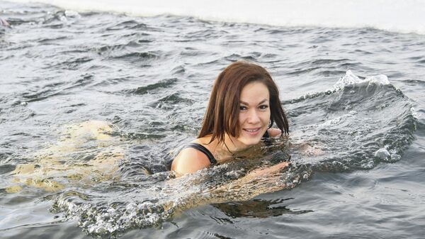 Девушка плавает в проруби. Купание в ледяной воде - популярный вид спорта и досуга у томичей зимой