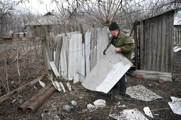 Мужчина расчищает территорию возле своего дома, разрушенную в результате обстрелов в поселке Финский в Горловке