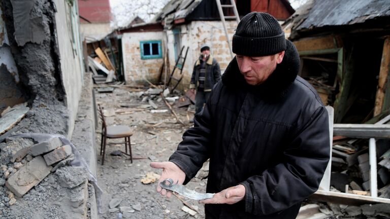Мужчина демонстрирует осколок возле дома поврежденного в результате обстрела ВСУ поселка Зайцево в Горловке