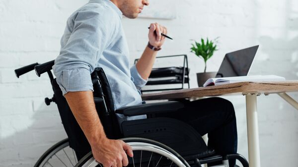 Мужчина в инвалидном кресле сидит за рабочим столом 