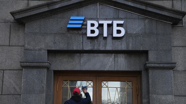 Сотрудник протирает стекла двери офиса ВТБ банка в Москве