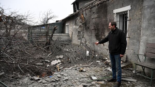 Мужчина демонстрирует последствия взрыва снаряда во дворе жилого дома на улице 9 января в Донецке