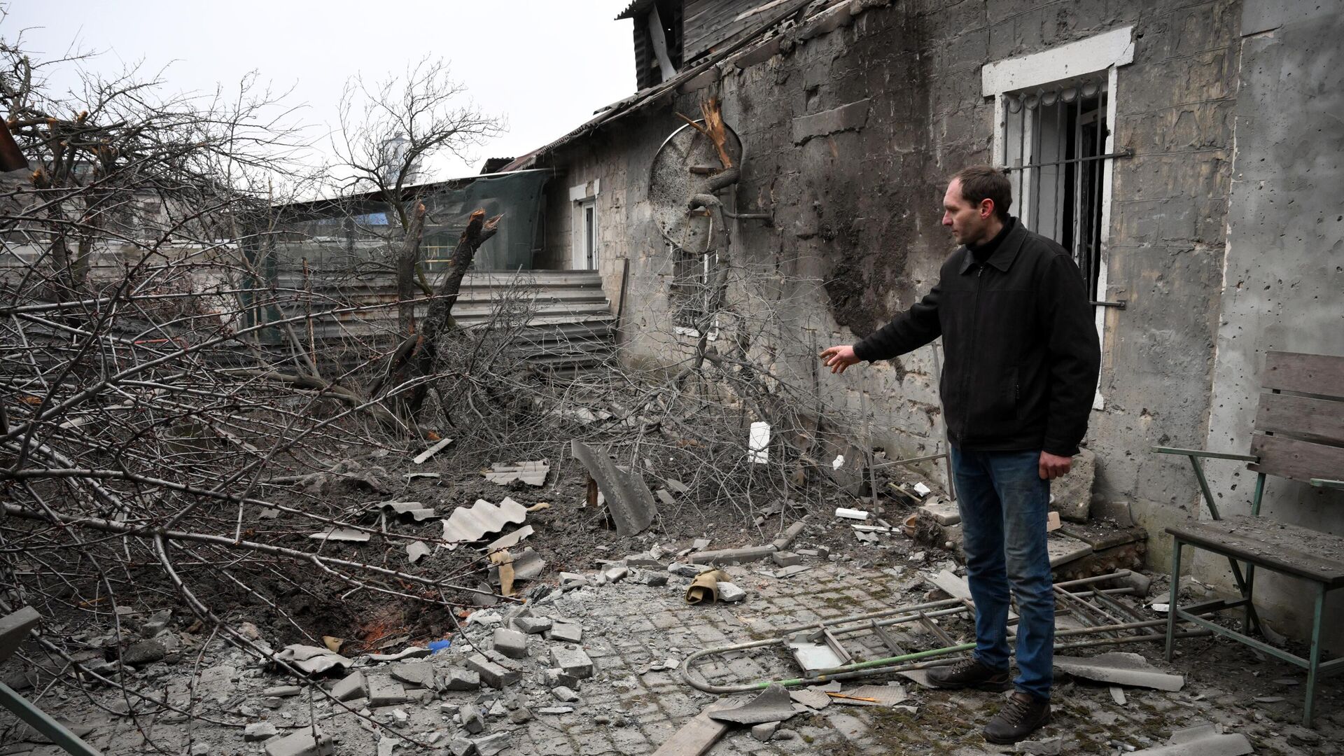 Мужчина демонстрирует последствия взрыва снаряда во дворе жилого дома на улице 9 января в Донецке - РИА Новости, 1920, 27.02.2022