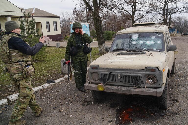 Военнослужащие народной милиции ДНР и ВС РФ возле машины, поврежденной в результате обстрела украинскими реактивными системами залпового огня в Николаевке