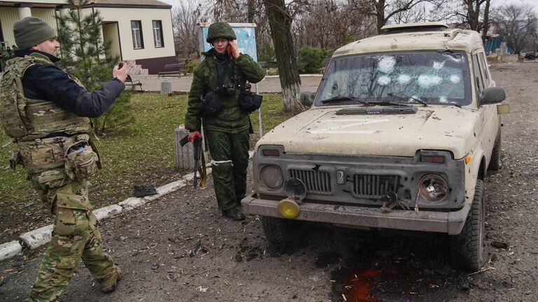 Военнослужащие народной милиции ДНР и ВС РФ возле машины, поврежденной в результате обстрела украинскими реактивными системами залпового огня в Николаевке