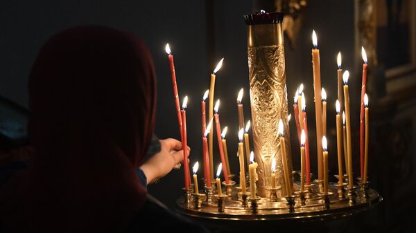 Верующая ставит свечу в храме 