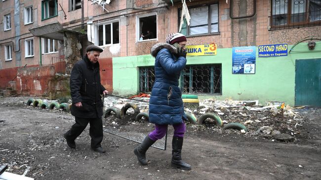 Люди идут вдоль дома, пострадавшего в результате обстрелов Горловки