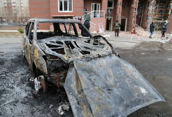 Сгоревший автомобиль во дворе многоэтажного жилого дома в Донецке, поврежденного в результате обстрела